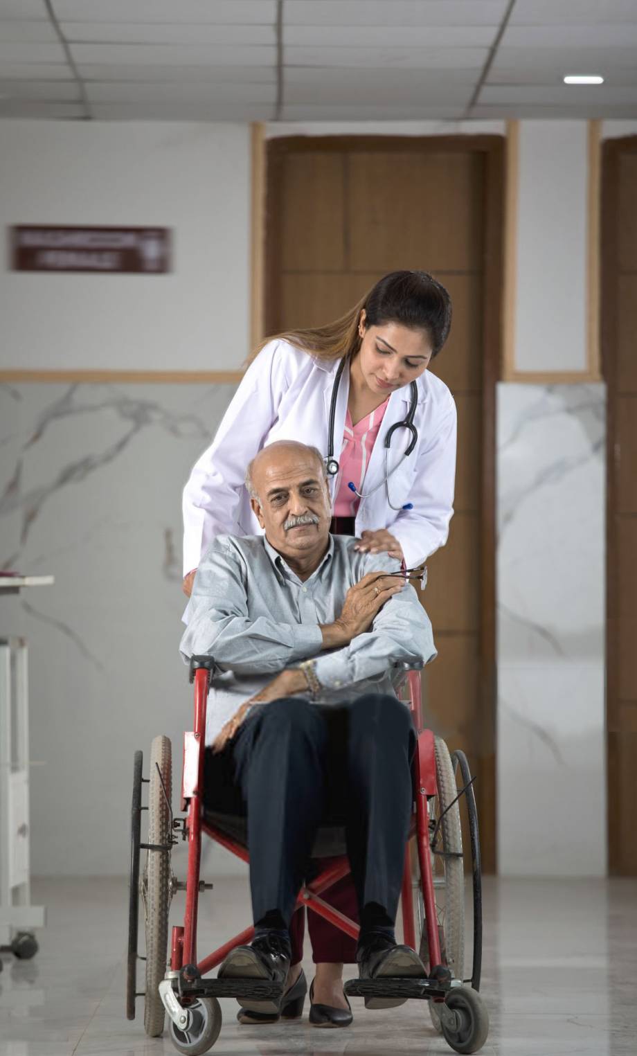 Female doctor consoling disabled old man in wheelchair at the hospital corridor